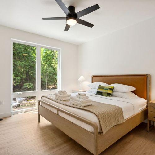 The second king bedroom offers minimalist design, a stylish wood-frame bed, and calming views of the forest—perfect for restful mornings and peaceful nights.