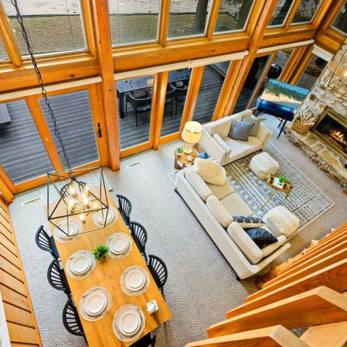 This bird's-eye view from the upper hallway captures the essence of the home's open-plan design, from the soaring ceiling and panoramic windows that flood the space with light, to the inviting living room that beckons with its cozy fireplace.