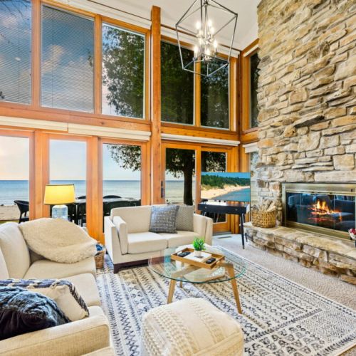 Expansive windows framing the picturesque beach and sky, the room bathes in natural light, enhancing the cozy yet modern decor. The space is designed for comfort and relaxation.