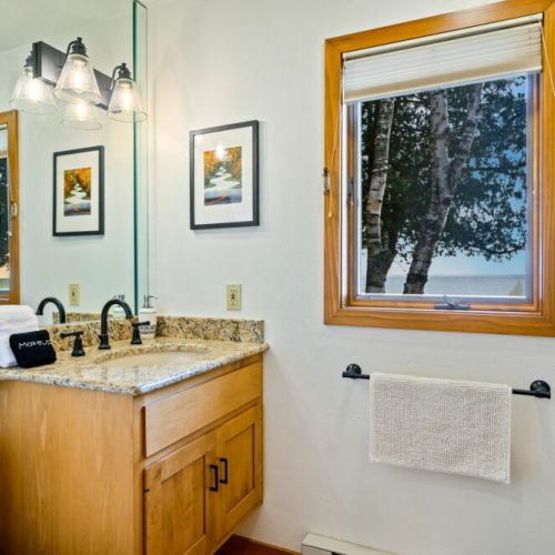 Well-appointed main-level bathroom with all the essentials for a rejuvenating experience. Granite countertop and warm wood cabinetry, complemented by a view of the water. Complete with a selection of high-quality toiletries.