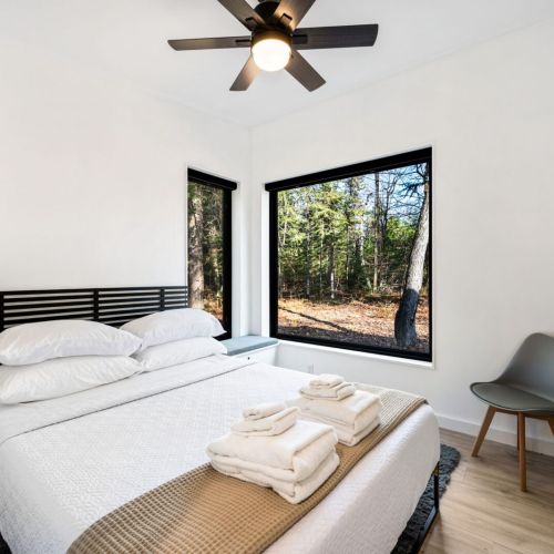 The bedroom includes a queen bed with plush linens, ensuring a restful night’s sleep. The large picture windows create the sensation of being completely surrounded by nature.