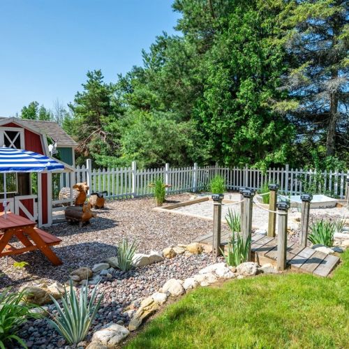 The natural play space features a dry "riverbed," miniature docks, a sunken rowboat, a barn playhouse, and a pea gravel digging area.