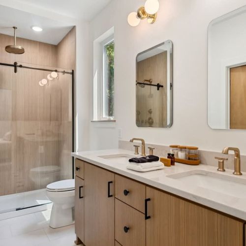 The en-suite bathroom offers a spacious walk-in shower with rainfall Kohler fixtures, double vanity, and soft lighting