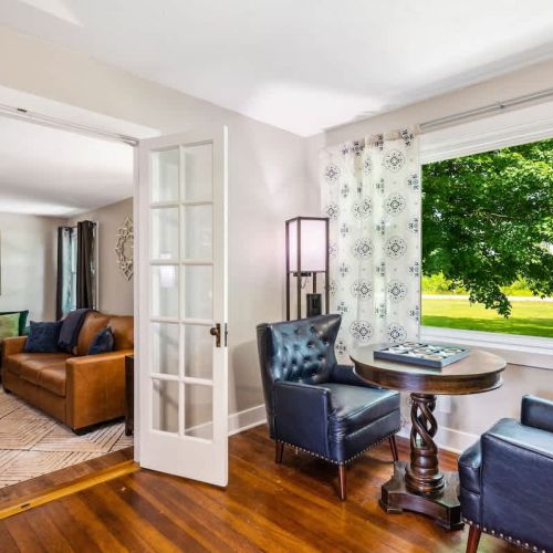 This cozy seating area offers a tranquil space with large windows overlooking lush greenery and comfortable leather chairs. Perfect for quiet moments or intimate conversations, it connects seamlessly to the main living room.  The sofa folds out to a