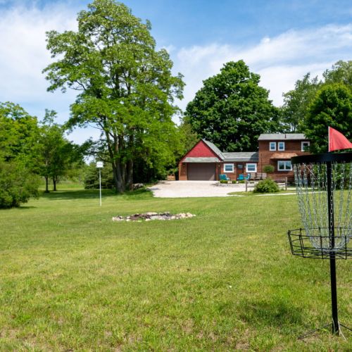 Enjoy the expansive outdoor space at Serenity Acres, complete with a fun disc golf setup and lush greenery. The charming house and well-maintained grounds provide the perfect backdrop for relaxation and outdoor activities.