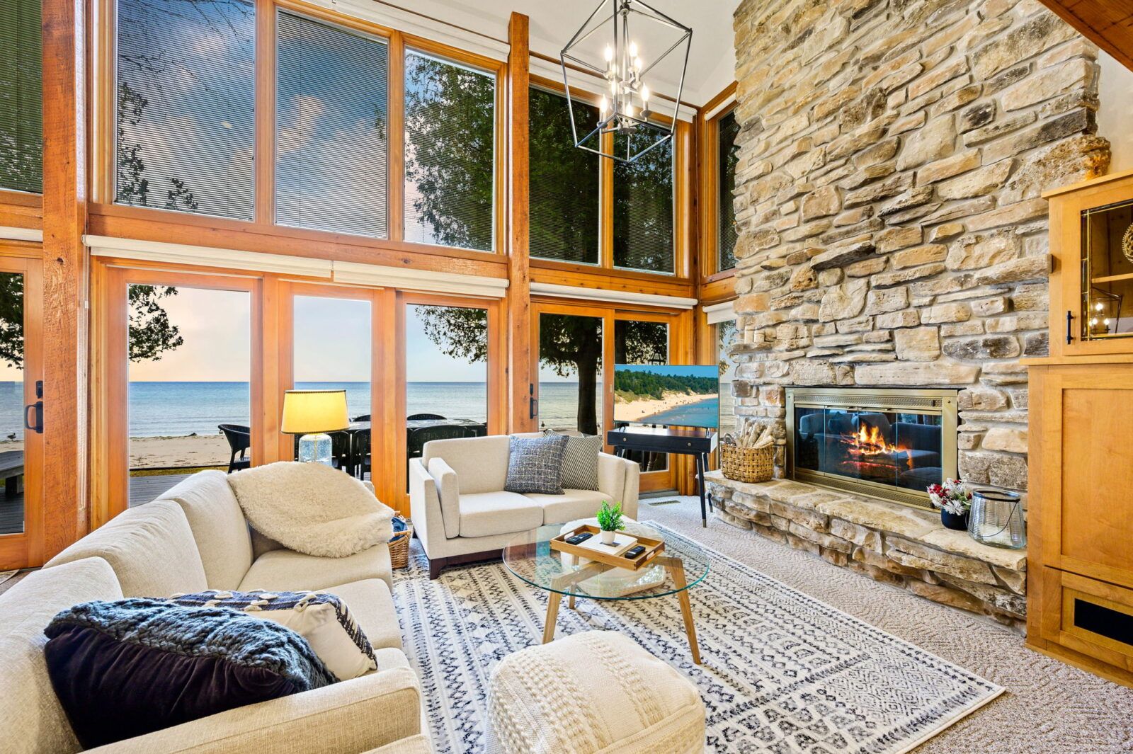 Expansive windows framing the picturesque beach and sky, the room bathes in natural light, enhancing the cozy yet modern decor. The space is designed for comfort and relaxation.